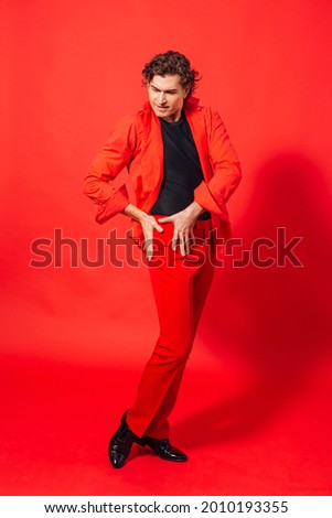 Portrait of a tall handsome man dressed in red shirt posing on the red background.