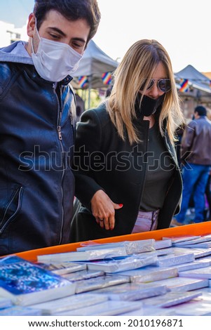 vertical photo latino hispanic man wearing medical masks with his partner a latina woman at a city fair, looking through books