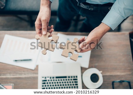 hand of businessman connecting jigsaw puzzle and laptop, coffee and document on the table. Business solutions, success and strategy concept