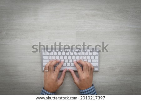 Hands and keyboard on white oak table Hands of an Asian businessman using a friend's wireless keyboard at home with copy space for text input. work from home concept far away from covid 19 top view