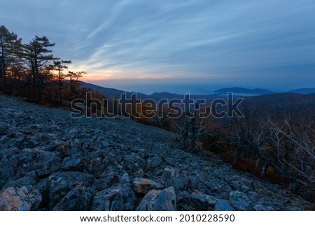 Sikhote-Alin Biosphere Reserve. The rocky slope of Mount Lysaya. A steep slope of a rocky mountain during a bright sunrise. Dry trees grow on a steep mountainside.