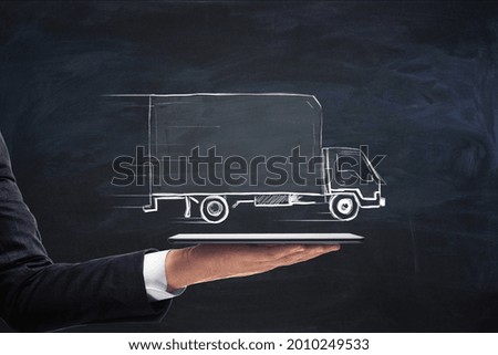 Businessman hand holding tablet with creative truck sketch. Transporation and logistics concept Royalty-Free Stock Photo #2010249533