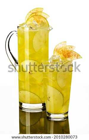 lemonade apple yellow or light green with apple slices and ice sprinkled with cinnamon in a glass and glass decanter in European style on white background