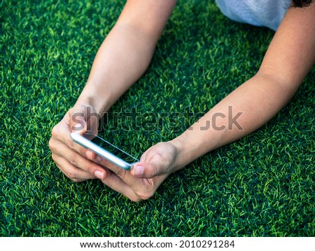 Close-up mobile phone in hands on green artificial grass background. Hands holding a smartphone, top view.