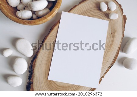 Boho vertical postcard mockup with white pebble and wooden cut section on white table background. Rustic bohemian image. Space for text. Good for handicrafts banners. Copyspace mockup