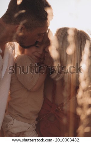 Young family, mother father and son hugging and kissing at sunset in summer 