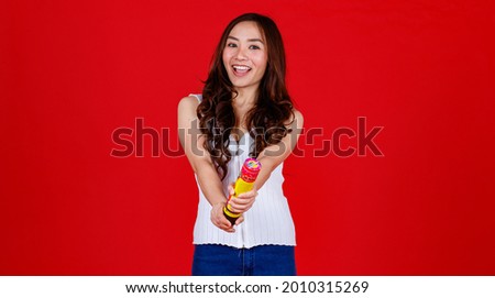 Funny young and cure Asian girl holding and blowing out party poppers with funny and happy. Studio shot on red background.