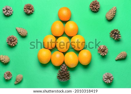Christmas tree made of oranges and pine cones on color background
