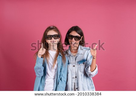 Modern mom and daughter in denim jackets on terracotta background in 3d cinema glasses positive smiling shows thumb up