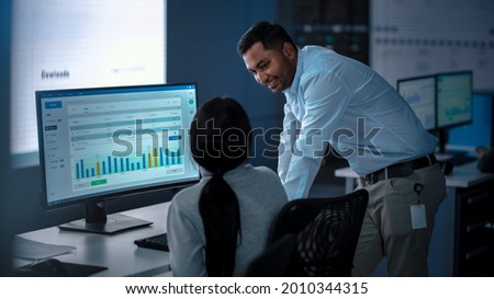 Two Professional Traders Taling and Working in a Modern Monitoring Office with Live Analytics Feed on a Big Digital Screen. Monitoring Room with Brokers and Finance Specialists.