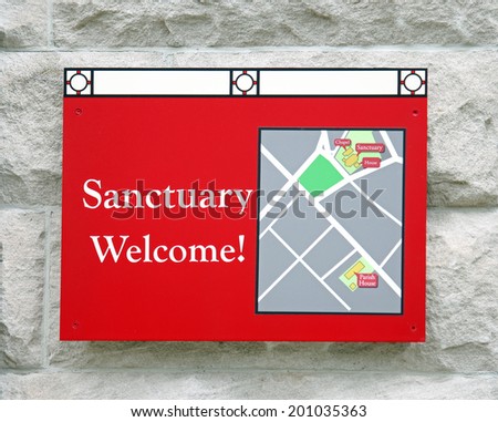 A red sign outside of a church reading  Sanctuary Welcome!