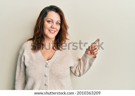 Young caucasian woman wearing casual clothes with a big smile on face, pointing with hand finger to the side looking at the camera. 