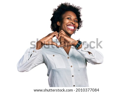African american woman with afro hair wearing casual white t shirt smiling in love doing heart symbol shape with hands. romantic concept. 