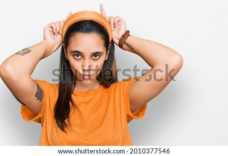 Young hispanic woman wearing casual clothes doing funny gesture with finger over head as bull horns 