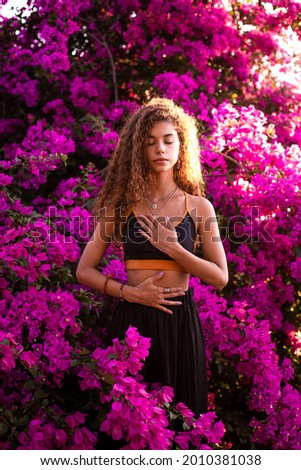 Brazilian young woman with curly hair making yoga pose at the sunset. Pink bougainvillea flowers at the background.
