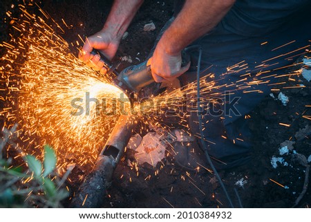 Worker cuts gas pipe with grinder and lots of sparks fly close up