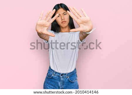 Beautiful young asian woman wearing casual white t shirt doing frame using hands palms and fingers, camera perspective 