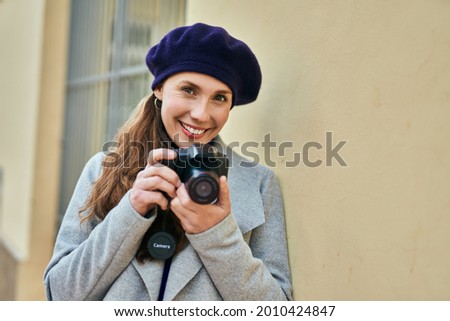 Young blonde woman smiling happy using reflex camera at the city.