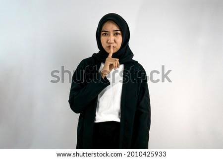 Beautiful asian young muslim woman with fingers on mouth, silence sign, do not make noise sign, do not speak, secret sign, warning sign, isolated on gray background