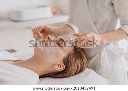Cosmetologist doing face treatment and applying face mask Royalty-Free Stock Photo #2010432491