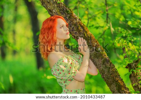Beautiful young woman standing among trees and looking into the distance. Warm summer day out of town