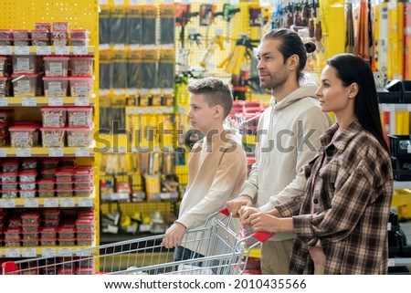 Young family of three pushing shopping cart with household goods