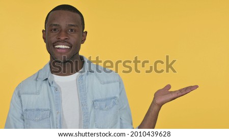 Young African Man Holding Product on Palm, Yellow Background 
