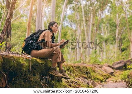 Biologist or botanist recording information about small tropical plants in forest. The concept of hiking to study and research botanical gardens by searching for information. Royalty-Free Stock Photo #2010457280
