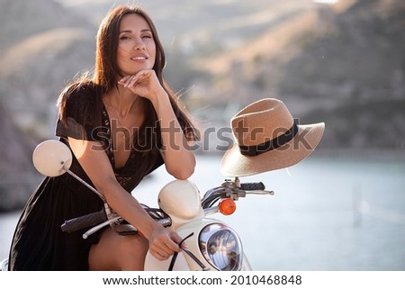 Beautiful young dark-haired girl traveler riding a scooter on the seashore. Travel and adventure concept.