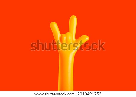 Photo of a plastic yellow colored hand sign gesture meaning I love you on orange background.