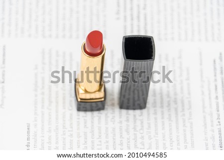 red lipstick of minimalist design in black and yellow packaging lies against the background of a fashion magazine