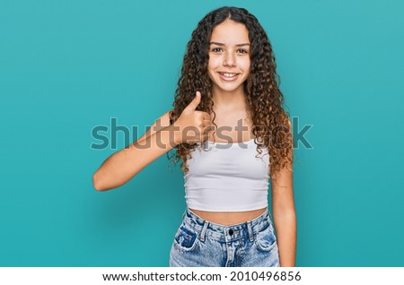 Teenager hispanic girl wearing casual clothes doing happy thumbs up gesture with hand. approving expression looking at the camera showing success. 