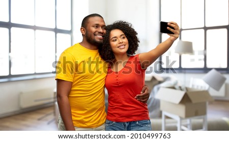 moving, real estate and people concept - happy smiling african american couple taking selfie by smartphone over new home background