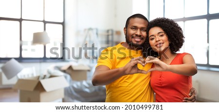 love, valentines day and moving concept - happy african american couple making hand heart gesture over new home background
