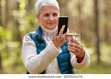 technology, leisure and people concept - senior woman with smartphone using app to identify mushroom in autumn forest