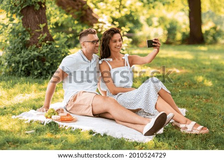 leisure and people concept - happy couple having picnic and taking selfie with smartphone at summer park