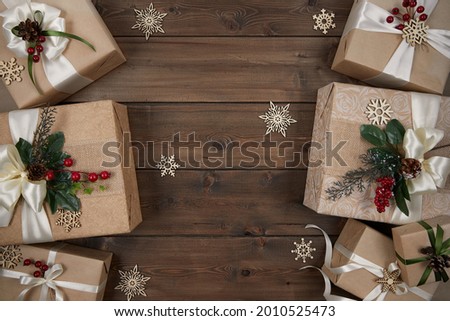 Rustic Christmas background with borders of gift boxes wrapped in kraft paper decorated with red berries and Christmas greenery on dark wood desk. Xmas, winter, holiday concept. Flat lay, copy space