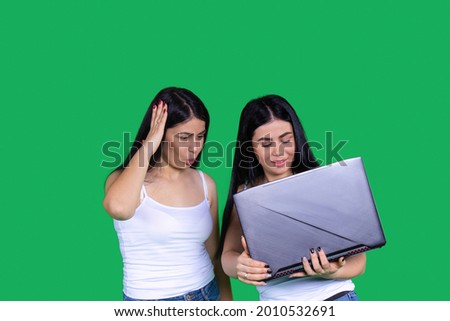 One of the twins is showing something interesting to another on the computer holding it in her hands.