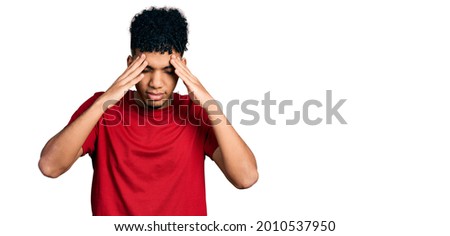 Young african american man wearing casual red t shirt with hand on head for pain in head because stress. suffering migraine. 