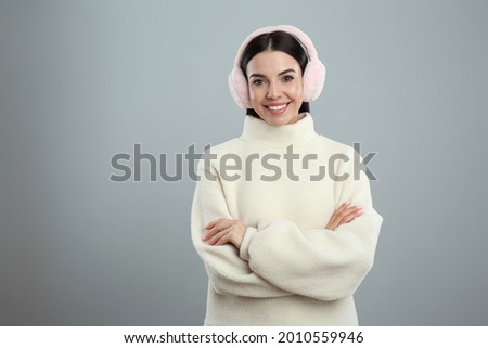 Beautiful young woman wearing earmuffs on light grey background. Space for text Royalty-Free Stock Photo #2010559946