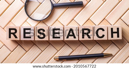 Wooden cubes with the word RESEARCH stand on a wooden background between a magnifying glass and a pen