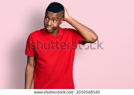 Young african american man wearing casual red t shirt confuse and wondering about question. uncertain with doubt, thinking with hand on head. pensive concept. 