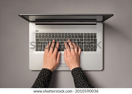 First person top view photo of female hands using laptop keyboard on isolated grey background