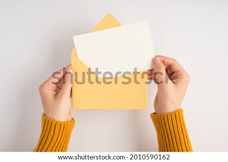 First person top view photo of female hands in yellow sweater holding open envelope with white card on isolated white background with blank space Royalty-Free Stock Photo #2010590162