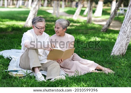 Happy old couple sitting on the park grass reading high quality photo