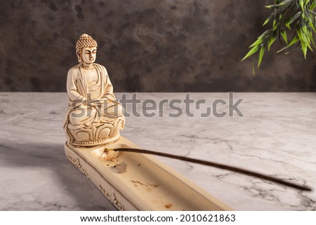 A closeup of an incense burner with a mini statue of Buddha 