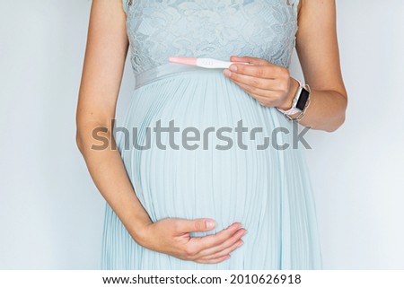 Closeup photography of young Woman holding positive pregnant test touching hand her big belly in blue dress Isolated on white background with copy space. Skin care with moisturising cream against