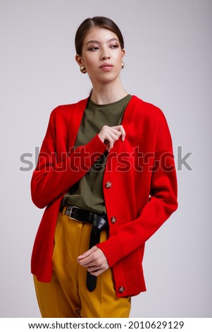 Fashion photo of a beautiful elegant young asian woman in a pretty yellow pants, red cardigan, green t-shirt, belt posing over white, soft gray background. Studio Shot.