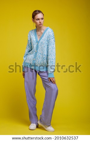 Fashion photo of a beautiful elegant young woman in a pretty walking suit, costume, lavender trousers, blue sweater blouse, sneakers posing yellow background. Studio Shot. Portrait