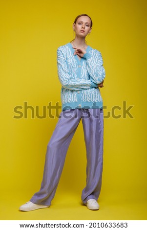Fashion photo of a beautiful elegant young woman in a pretty walking suit, costume, lavender trousers, blue sweater blouse, sneakers posing yellow background. Studio Shot. Portrait
